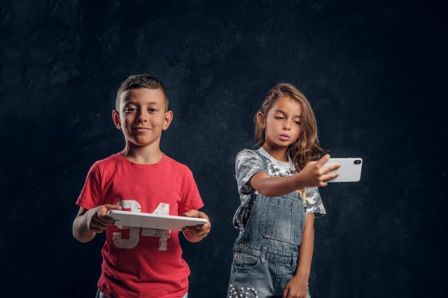 redimensionner happy smiling boy is holding tablet while girl is making selfie by mobile phone